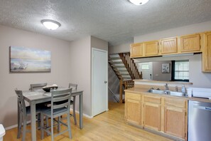 Una cocina con armarios de madera, una mesa de comedor con sillas, una escalera y un cuadro en la pared.