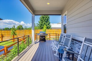 Eine überdachte Terrasse mit Grill, Gartenmöbeln und Blick auf Baum und Zaun.