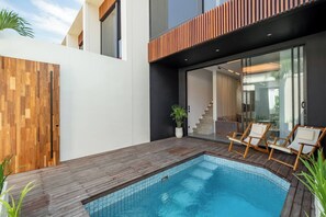 Ein moderner Poolbereich im Freien mit Holzdeck, Liegestühlen und einer Glastür, die zu einer Treppe führt.