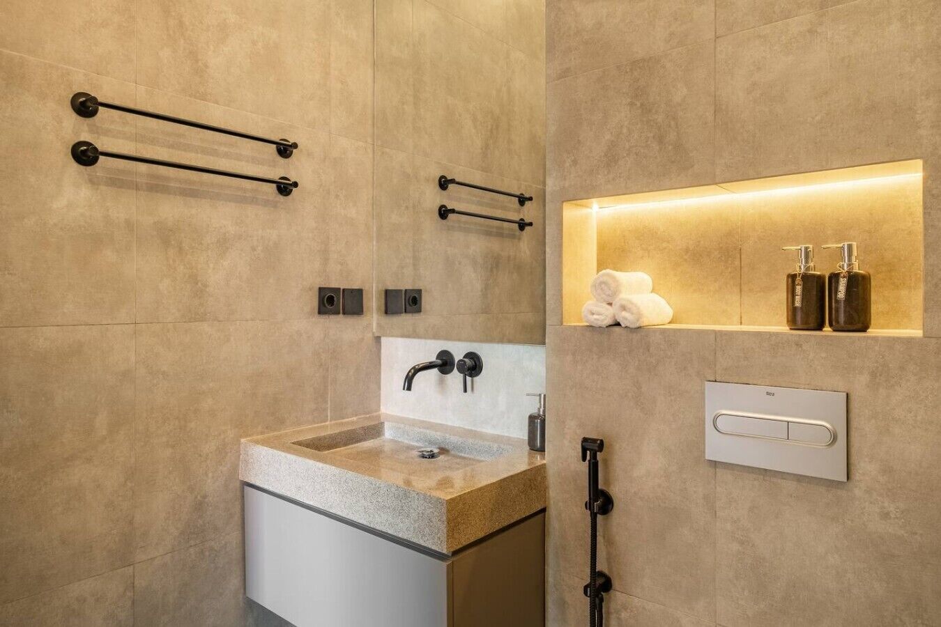 Uma casa de banho moderna com lavatório de granito, torneira embutida na parede, suportes para toalhas e um armário com artigos de higiene pessoal.
