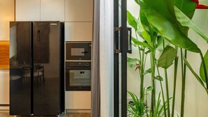 Uma cozinha com geladeira preta, micro-ondas e forno. Há uma porta de vidro que dá para uma sala de jantar.