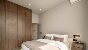Quarto moderno com uma cama grande, guarda-roupa de madeira, mesas de cabeceira e um aparelho de ar condicionado.
