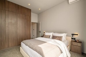 Ein modernes Schlafzimmer mit einem großen Bett, einem Holzschrank, Nachttischen und einer Klimaanlage.