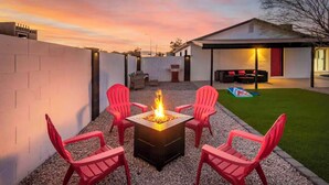 Une terrasse avec un foyer, quatre chaises rouges et une maison en arrière-plan.