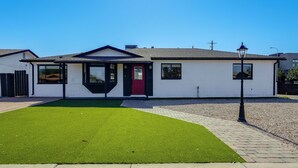 Une maison de plain-pied avec une porte rouge, un petit jardin devant la maison avec de l’herbe artificielle et un lampadaire.