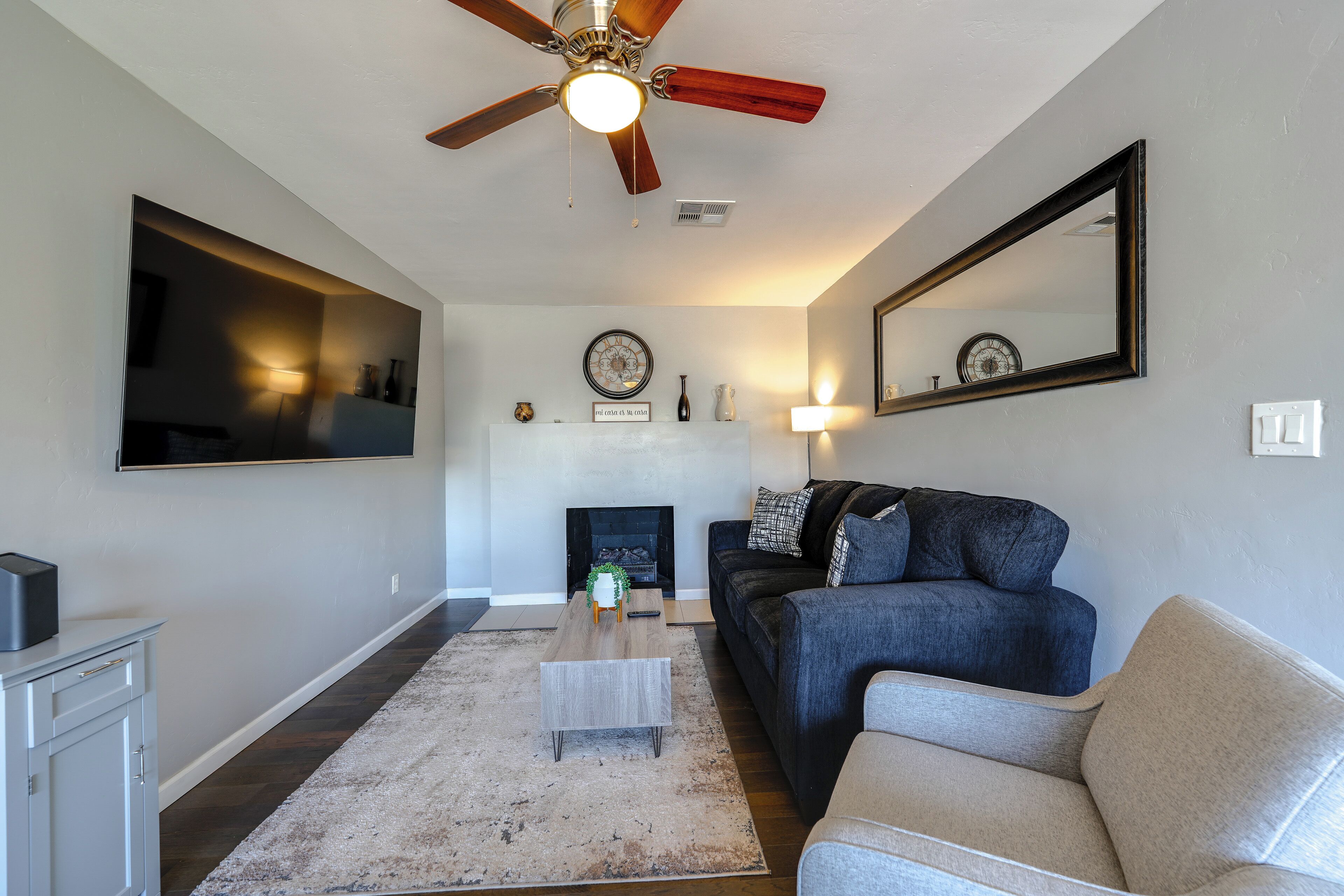 A living room with a ceiling fan, a fireplace, a sofa, a coffee table, and a TV mounted on the wall.