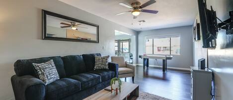 A living room with a dark blue sofa, a wooden coffee table, a ceiling fan, and a large window.