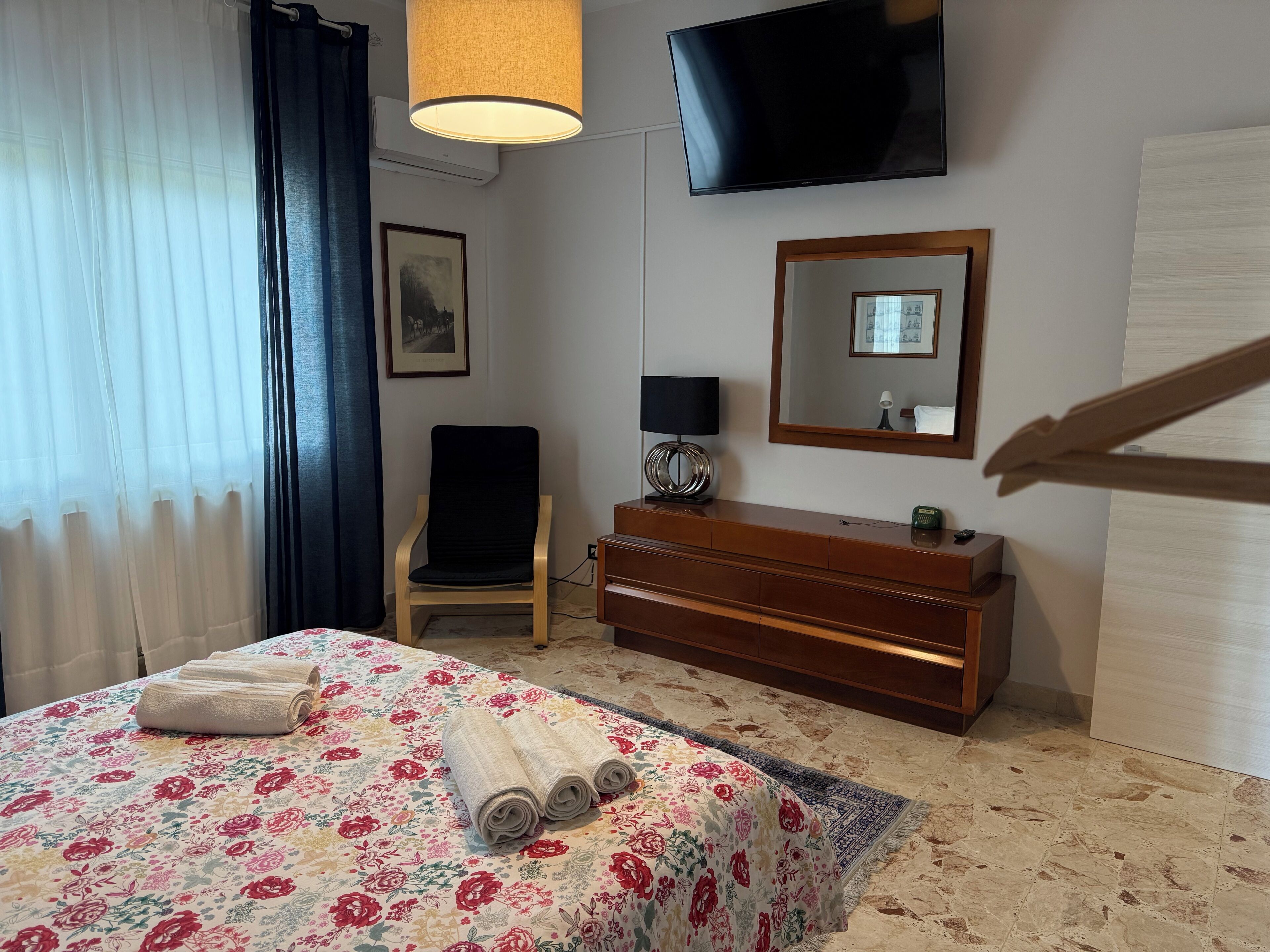 Hotellihuone, jossa on sänky, lipasto, tuoli, televisio ja peili.