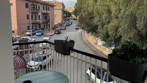 Un balcón con mesa y sillas, que da a una calle con coches y edificios.