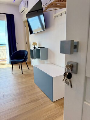 A modern living room with a flat-screen TV mounted on the wall, a blue sofa, a wooden floor, and a door with a key hook.