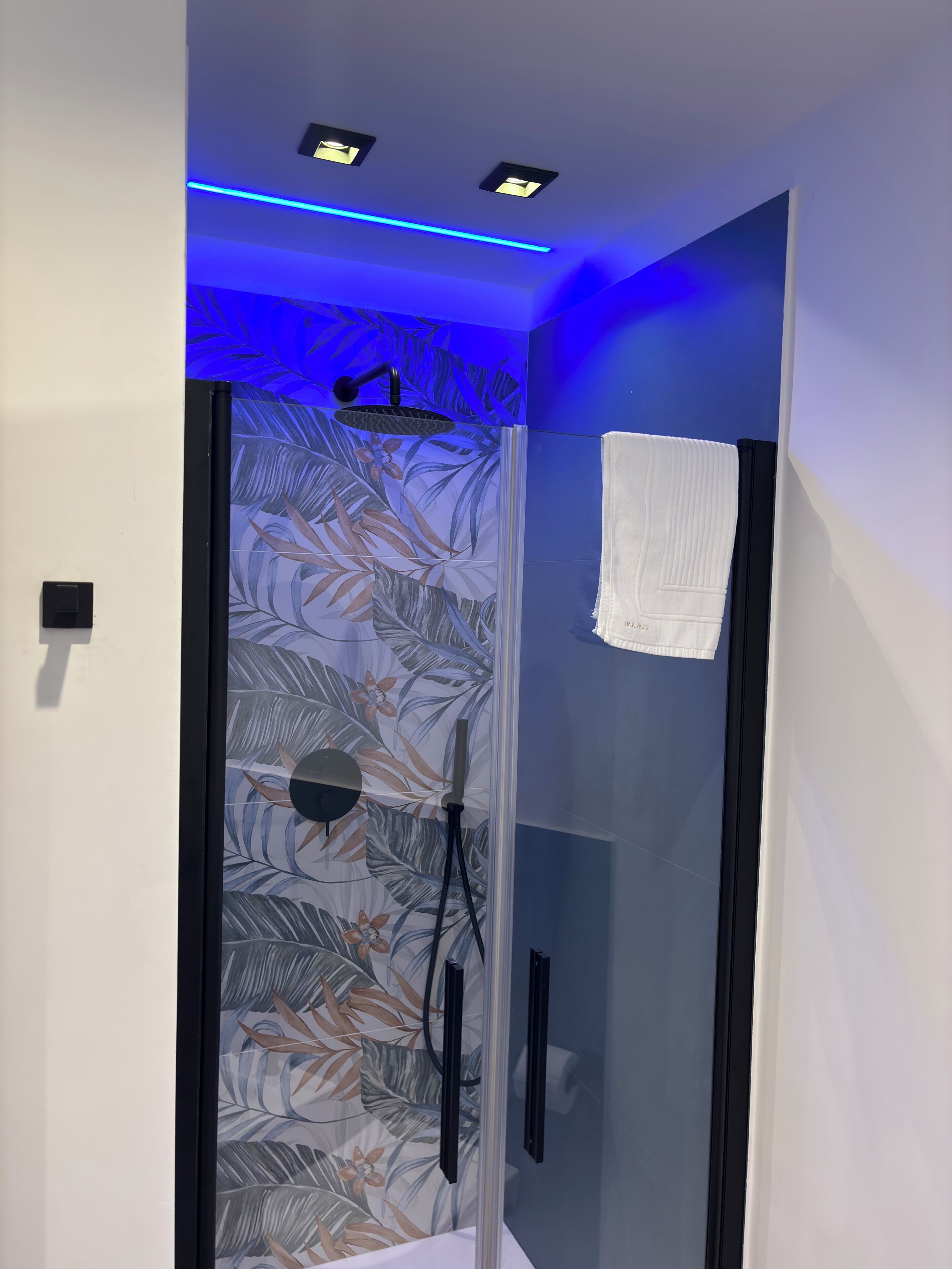 Eine moderne Dusche mit Glastür, einem Handtuch und einer Decke mit blauem LED-Licht.