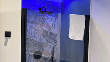 Eine moderne Dusche mit Glastür, einem Handtuch und einer Decke mit blauem LED-Licht.