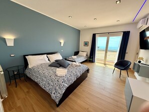 A bedroom with a bed, a desk, a chair, a TV, and a balcony with a view.