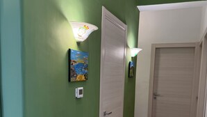 Un pasillo con paredes verdes, suelo de baldosas, una puerta y dos lámparas fijadas a la pared.