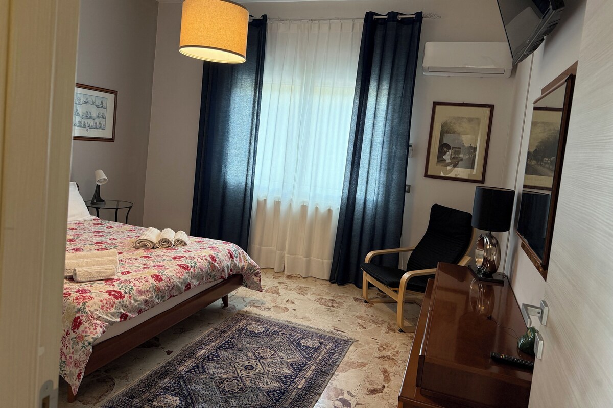 Habitación de hotel con cama, escritorio, silla, alfombra, televisor y cortinas.