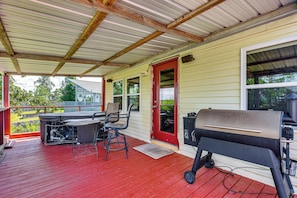 Een overdekt terras met een barbecue, een tafel en stoelen.
