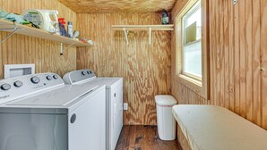 A laundry room with a front-loading washer and dryer, wooden walls, a window, and shelves with cleaning supplies. - On Deer Point Lake! Home w/ Private Dock & Hot Tub (Youngstown)