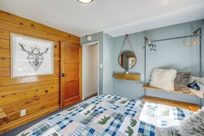 Ein Schlafzimmer mit Holztür, einem gerahmten Tierbild, einem hängenden Spiegel, einem Regal mit einer Pflanze und einer Steude auf dem Bett.