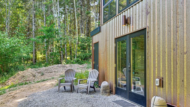 Un edificio moderno con un patio de grava, dos sillas Adirondack y una escultura de piedra.