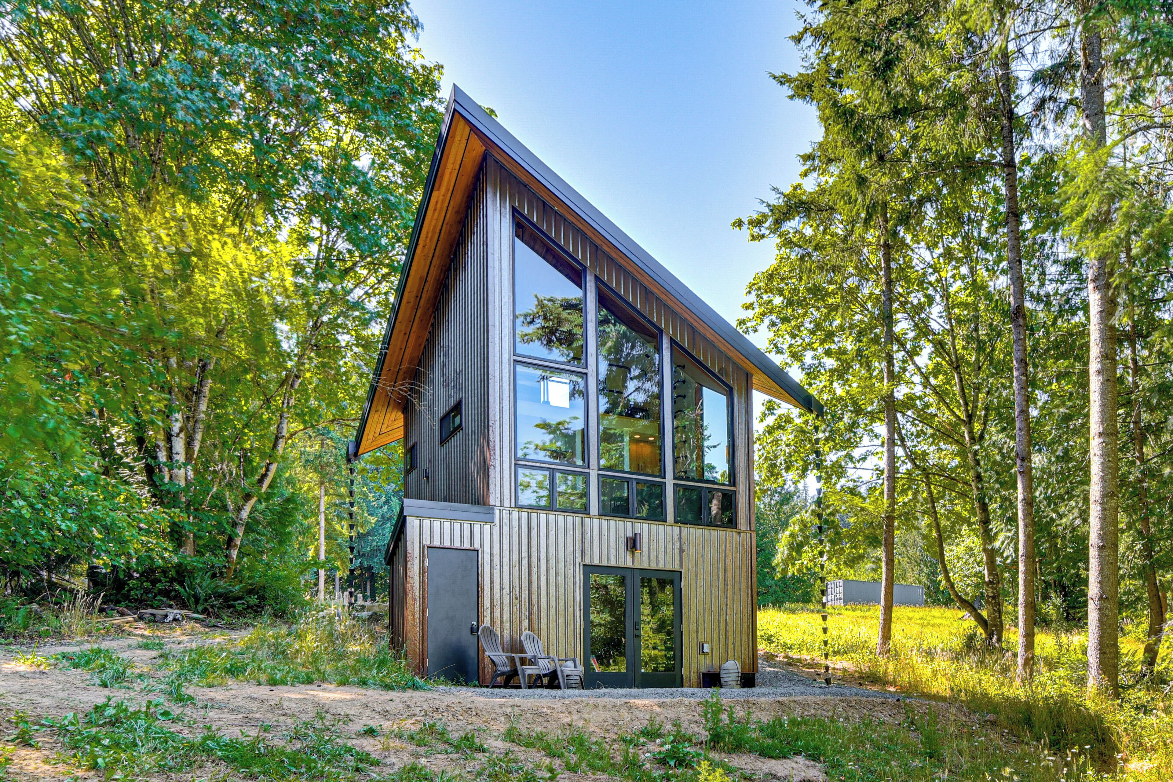 Een moderne cabin met een grote glazen gevel, omgeven door een bos.