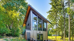 Una cabaña moderna con un amplio ventanal, rodeada de bosque.