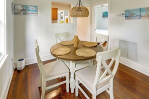 Un coin repas avec une table ronde, des chaises blanches, des sets de table en fibres tressées et un luminaire suspendu également en fibres tressées.