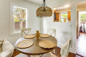 A dining area with a round wooden table, four woven placemats, white chairs, and a woven pendant light. - Walk to Lakeworth Dtwn! 5-Min Drive to Beach (Lake Worth Beach)