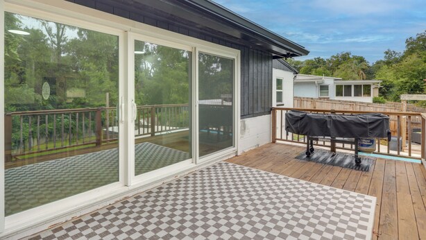 Een overdekt terras met een geruit vloer, een barbecue en een schuifpui naar een zwembad.