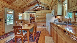 Interior de una cabaña de madera con comedor, cocina y habitación en el altillo.