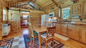 Interior de una cabaña de madera con comedor, cocina y habitación en entrepiso.