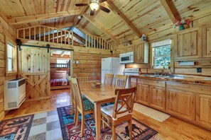 Ein Holzblockhaus-Innenraum mit Essbereich, Küche und einem Schlafzimmer auf der Galerie.