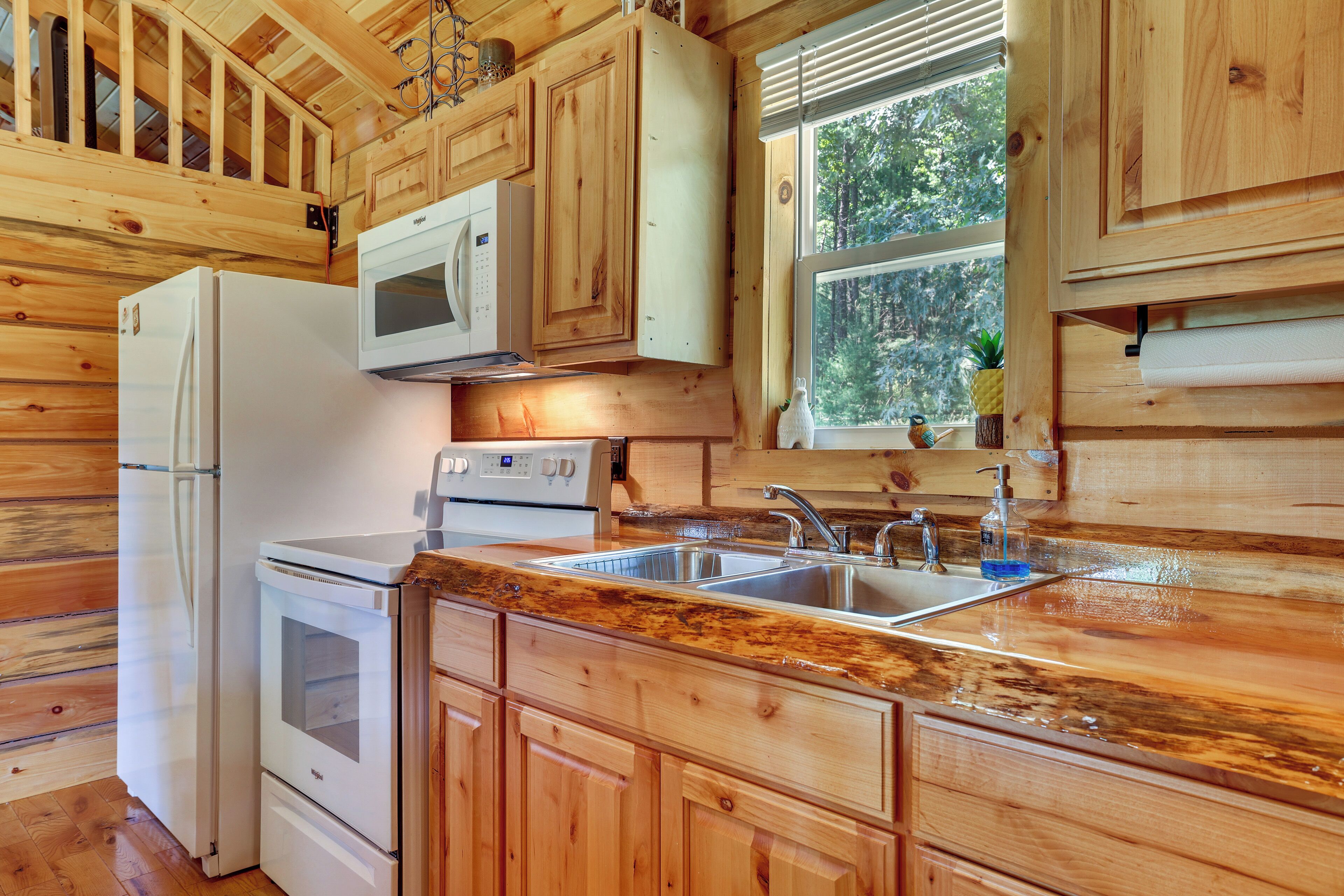 A kitchen with wooden cabinetry, a stainless steel sink, and a window with a view of trees.