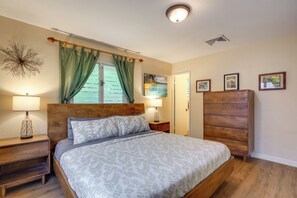 A bedroom with a wooden bed, two bedside tables, a nightstand, a wooden wardrobe, and a window with green curtains. - Walk to Sunset Beach! Extended Escape w/ Patio (Haleiwa)