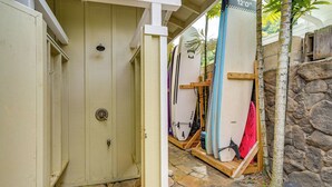 Een overdekt gebied met surfplanken, een stenen muur en een houten deur.