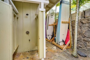 A covered area with surfboards, a stone wall, and a wooden door. - Walk to Sunset Beach! Extended Escape w/ Patio (Haleiwa)