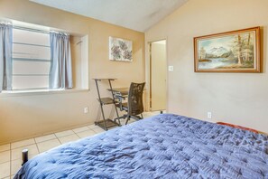 A bedroom with a bed, a desk, and a chair. There is a window with curtains, a painting on the wall, and a door. - Shop, Dine & Explore: El Paso Escape w/ Patio (El Paso)