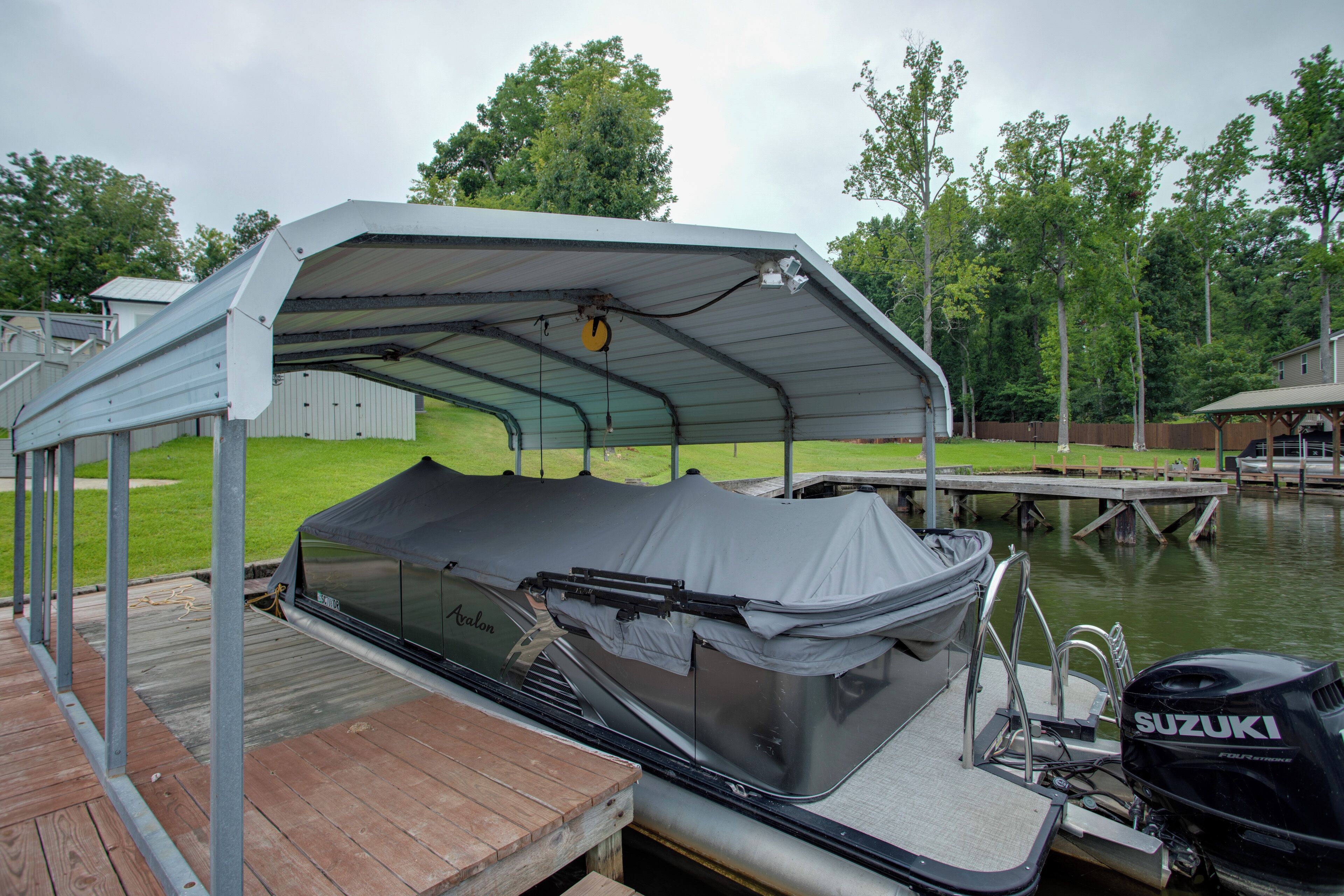 A covered boat dock with a Suzuki outboard motor, a covered seating area, and a wooden dock.