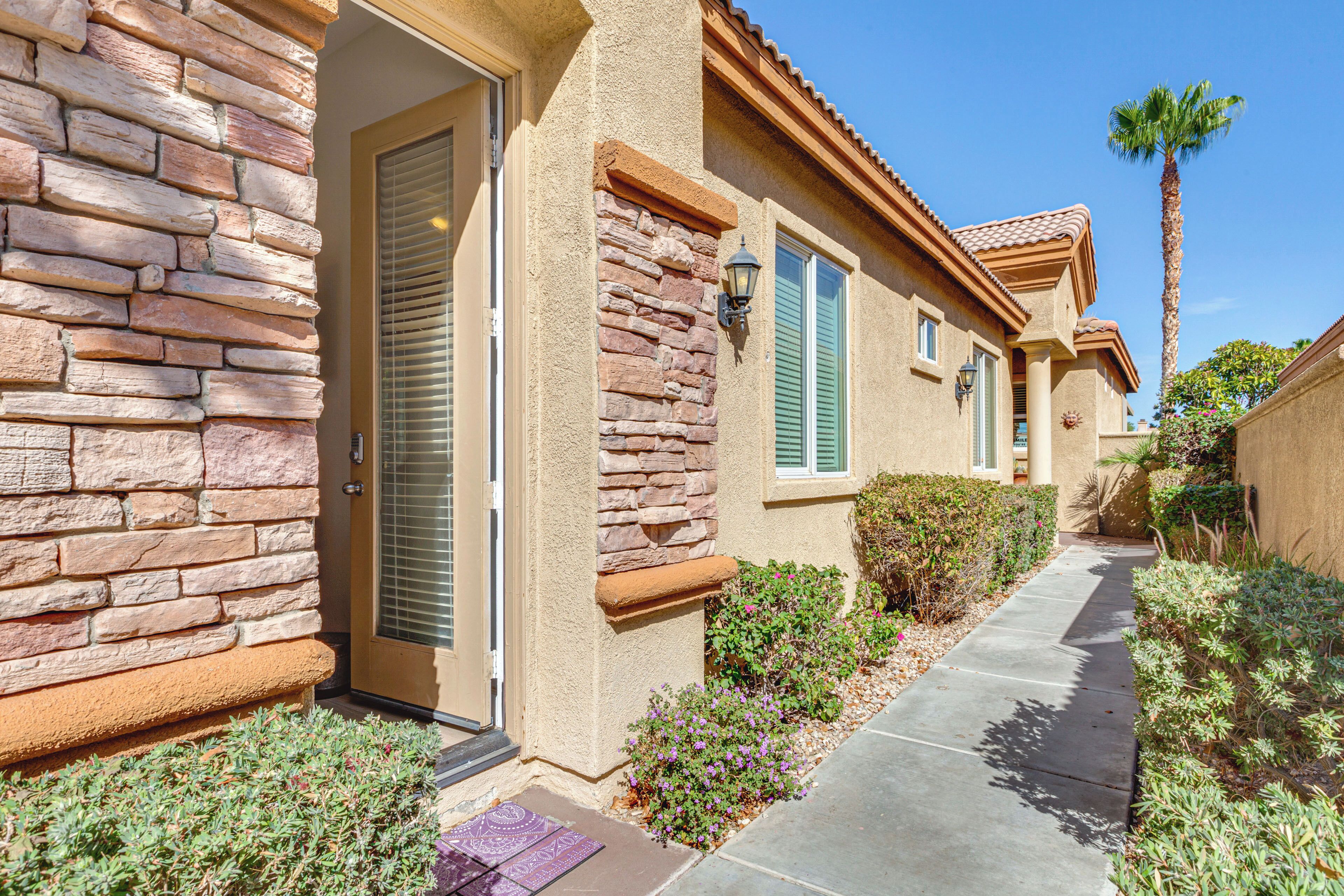 A residential building with a stone facade, a door, a window with shutters, a pathway, and a palm tree.