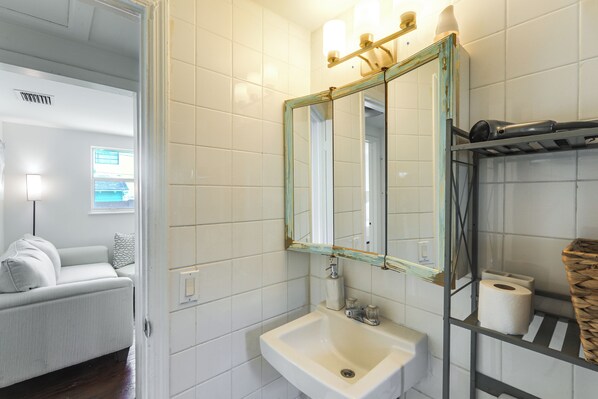 A bathroom with a sink, mirror, and shelves with toiletries. - Walkable Dtwn Spot! Bright Bungalow Near Beach (Lake Worth Beach)