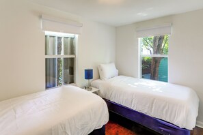 A bedroom with two beds, a nightstand, a lamp, and windows with curtains. - Walkable Dtwn Spot! Bright Bungalow Near Beach (Lake Worth Beach)