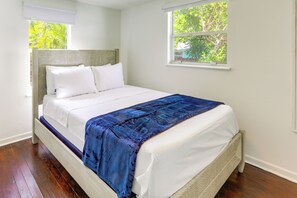 A bed with white bedding and a blue blanket, a wooden headboard, and a window with a view of trees. - Walkable Dtwn Spot! Bright Bungalow Near Beach (Lake Worth Beach)