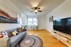 Ein modernes Wohnzimmer mit einer Couch, einem Fernseher, einem Deckenventilator und einem Essbereich im Hintergrund.