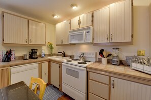 A kitchen with white cabinets, a stove, a microwave, and various appliances. - Charming 1870s Carriage House in Historic Downtown (Savannah)