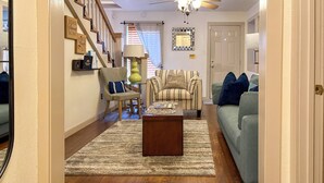 A living room with a sofa, armchair, coffee table, and a staircase with wooden railings. - Charming 1870s Carriage House in Historic Downtown (Savannah)