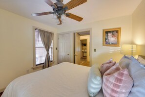 A bedroom with a large bed, a ceiling fan, a door leading to a bathroom, and a framed picture on the wall. - Charming 1870s Carriage House in Historic Downtown (Savannah)