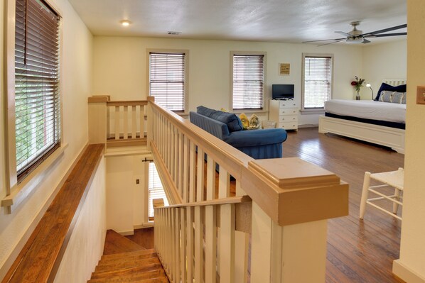 A spacious room with a wooden staircase, a bed, a sofa, and a television. - Charming 1870s Carriage House in Historic Downtown (Savannah)