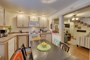 A kitchen with white cabinets, a microwave, stove, and a dining area with a table and chairs. - Charming 1870s Carriage House in Historic Downtown (Savannah)