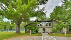 Une maison à deux étages, avec un grand arbre devant, une allée et un court de tennis à l’arrière.