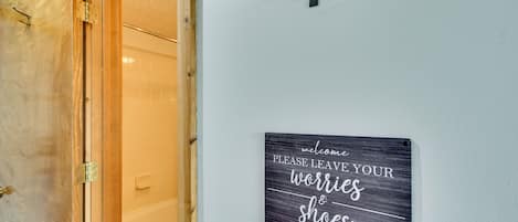 A bathroom with a wooden door, a towel rack, and a wall-mounted sign with a humorous message.