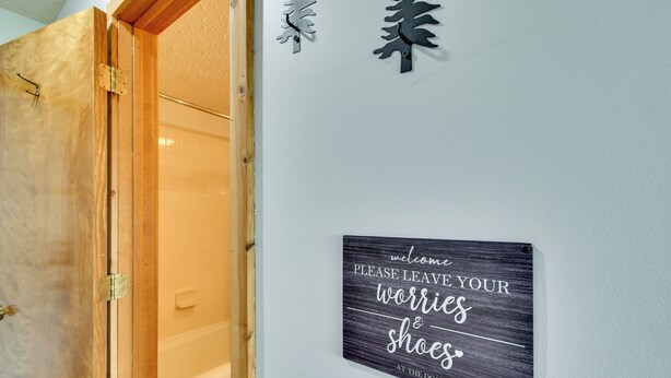 Une salle de bain avec une porte en bois, un porte-serviettes et un panneau fixé au mur portant un message humoristique.